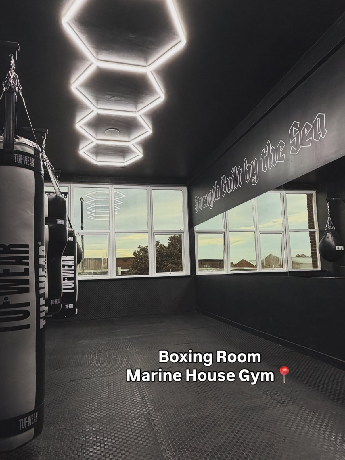 Heavy bags hanging in the boxing room beneath the Strength Built by the Sea wall script